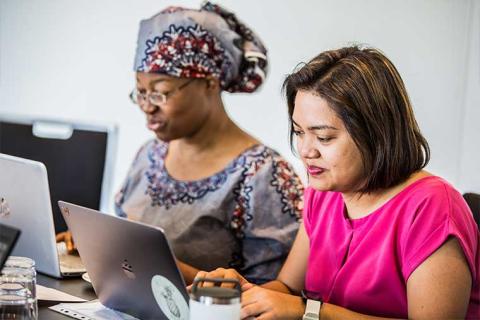 Rachel Devotsu and Evita Ricafort looking over their laptopts while preparing a McCabe Centre training