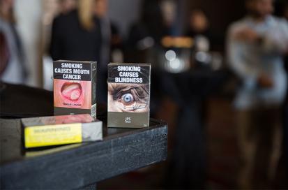 Plain packaging in Australia - tobacco packages in drab dark brown packaging with large graphic health warnings, one with a picture of a tumor and text saying Smoking Causes Mouth Cancer, another with a picture of a damaged eye saying Smoking causes blindness 